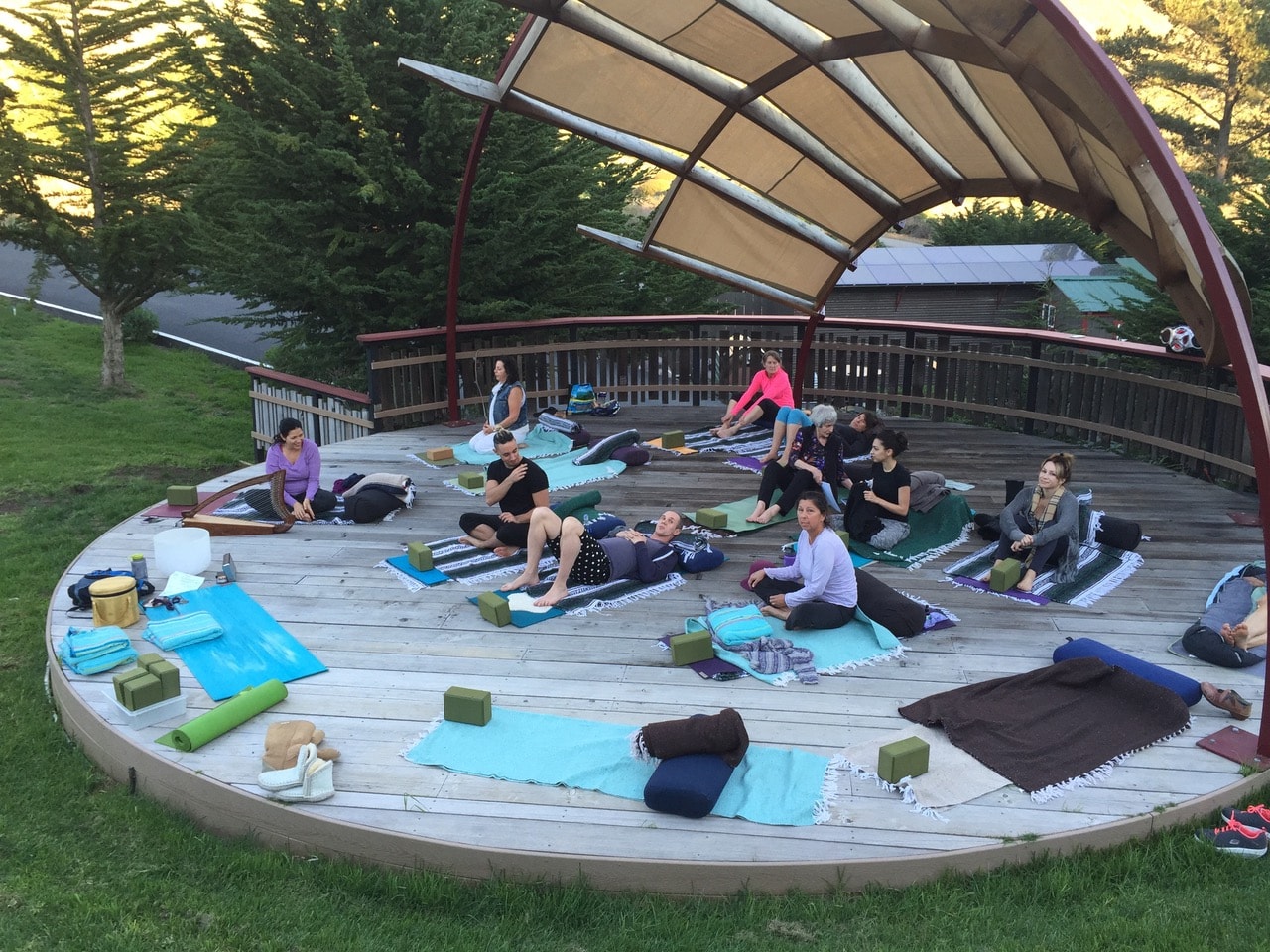 Group yoga practice on an outdoor wooden deck beneath a canopy